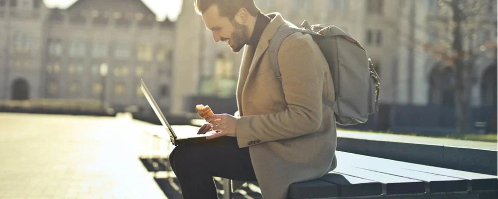 Sac Ă dos ordinateur homme utilisĂ© en extĂ©rieur sur un campus universitaire, homme assis avec laptop sur les genoux, profitant dâun moment connectĂ© en plein air