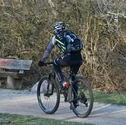 Sac à dos Sport - Cycliste en tenue noire et verte transportant un sac à dos compact sur un sentier forestier, vélo tout terrain en mouvement