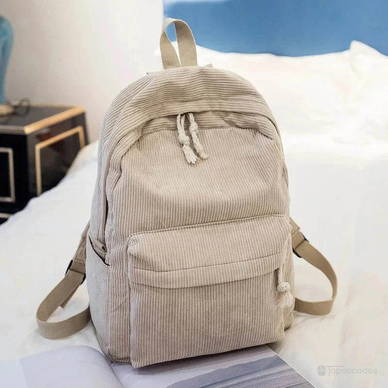 sac à dos college en velours cotelé beige avec cordons blancs, posé sur un lit dans une chambre moderne