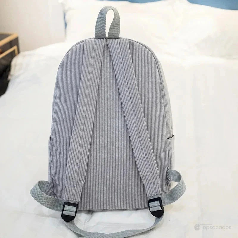 sac à dos college en velours cotelé gris vu de dos avec bretelles réglables sur un lit blanc