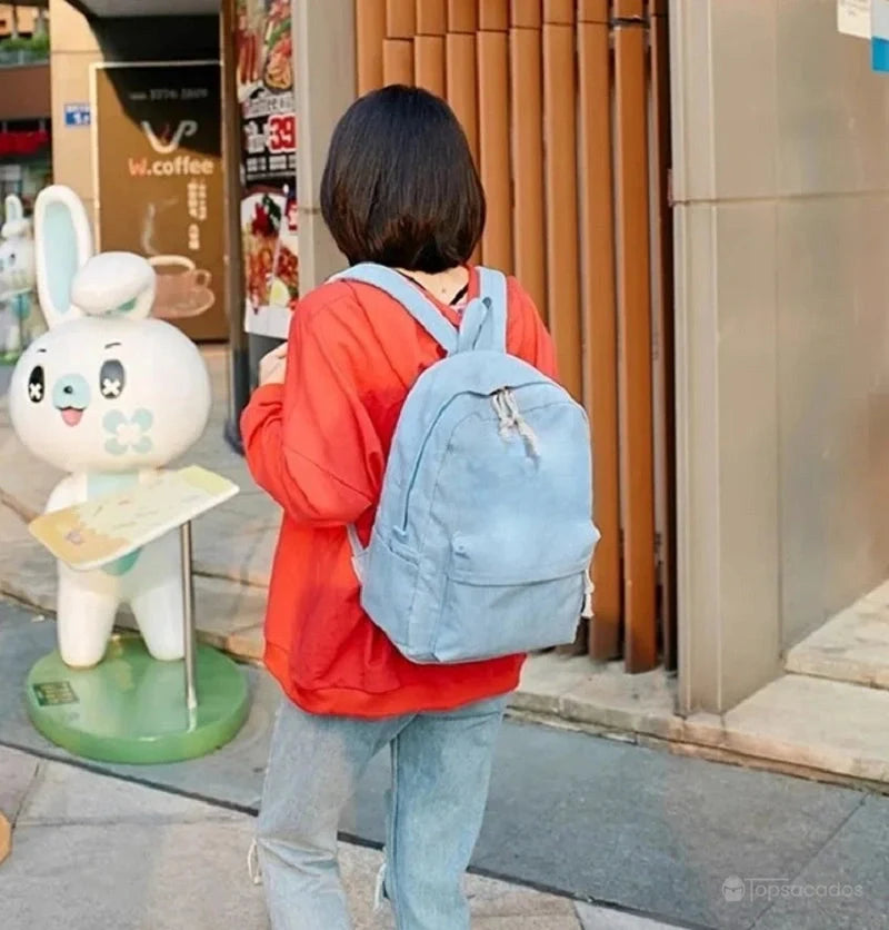 sac à dos college en velours cotelé bleu clair porté en extérieur par une jeune femme en sweat rouge, devant un café urbain