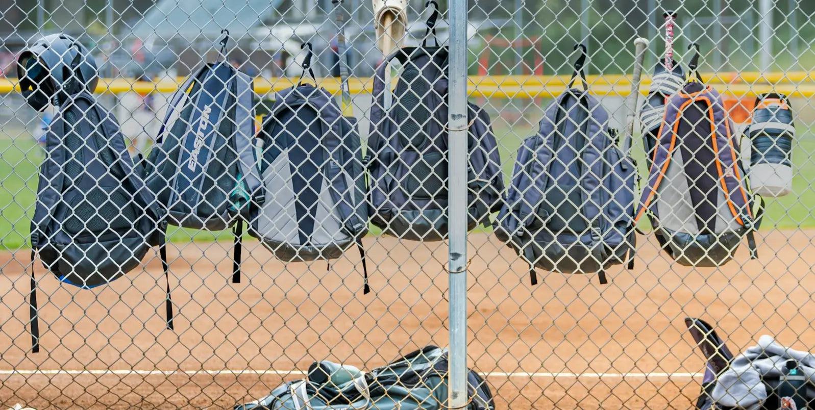 Rangée de sacs à dos enfant suspendus à une clôture de terrain de baseball, chaque sac contenant des équipements sportifs, ambiance de match en plein air.