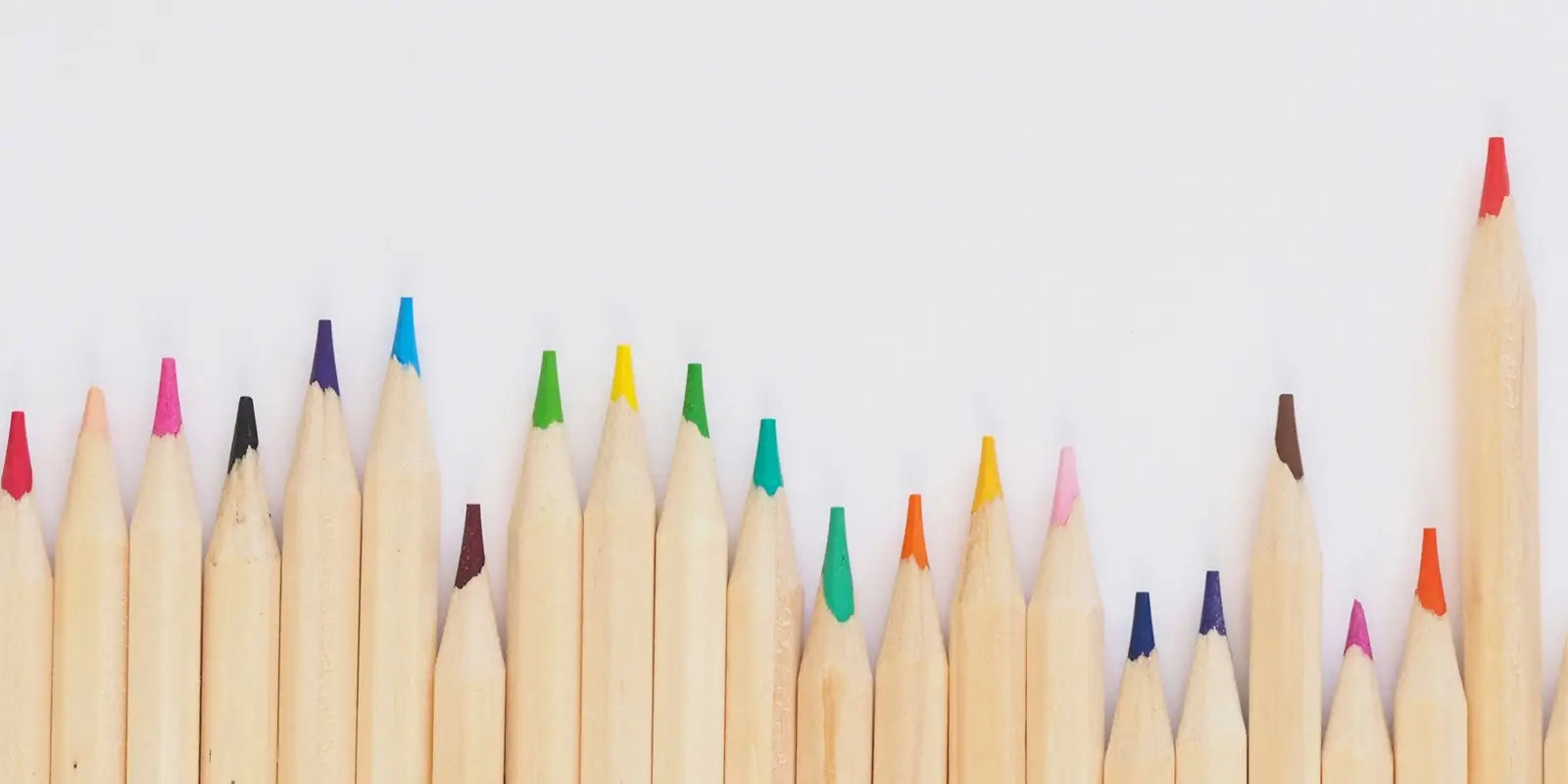 Crayons de couleur en bois non verni alignés sur fond blanc, accessoires scolaires pour enfants de maternelle.