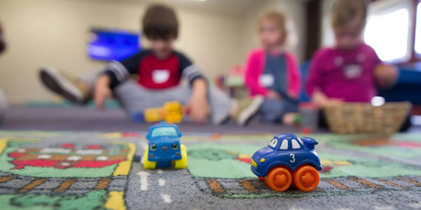 Activités maternelle avec enfants jouant sur un tapis éducatif et voitures en plastique colorées.