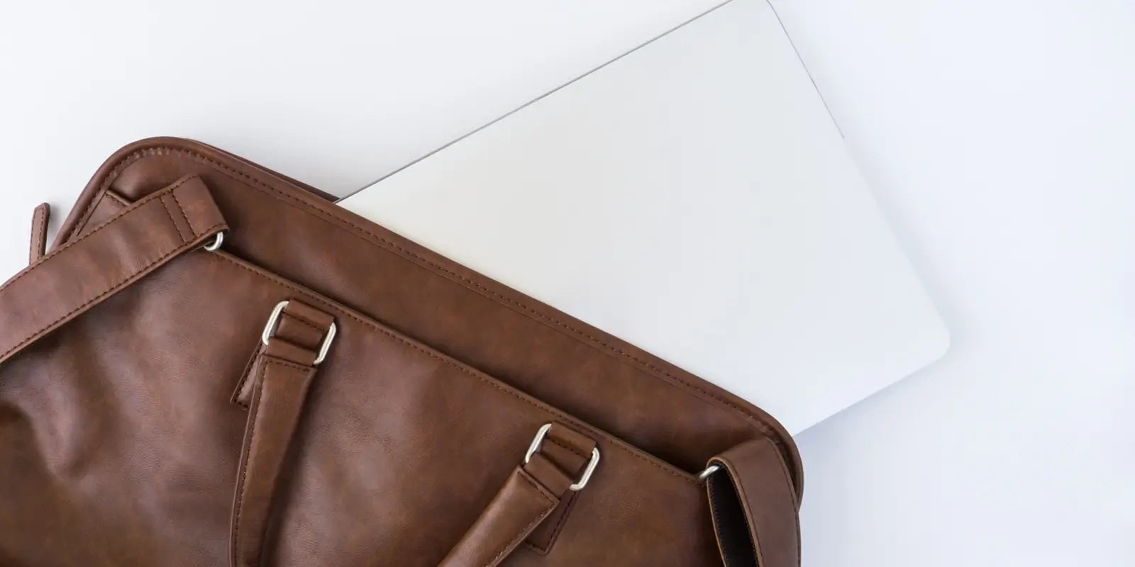 Ordinateur portable glissé à moitié dans un sac à dos ordinateur portable en cuir marron, posé sur un fond blanc épuré, mettant en valeur le design élégant et professionnel du sac.