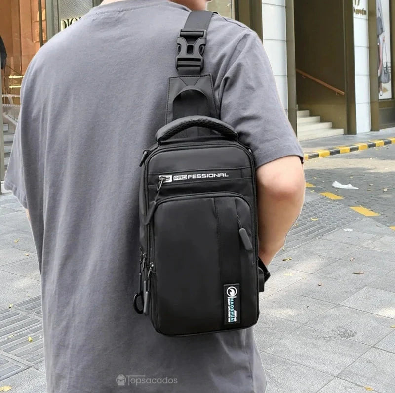 Petit sac à dos homme noir porté sur l'épaule dans la rue, vu de dos, environnement urbain avec vitrines en arrière-plan.