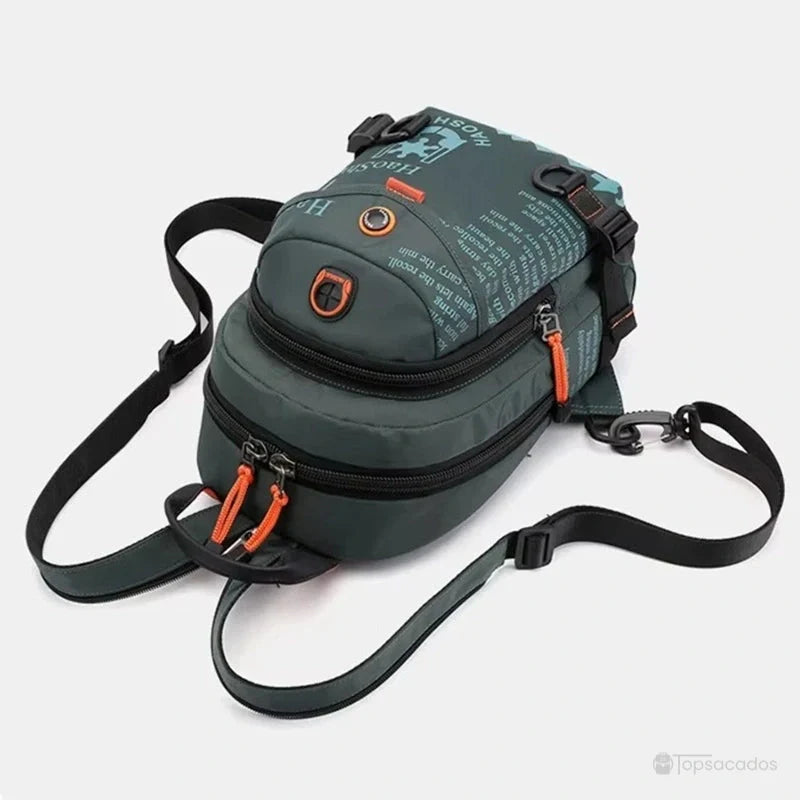 Petit sac à dos vert vu de dessus avec fermetures orange, bretelles ajustables et sortie casque audio, posé sur fond clair.