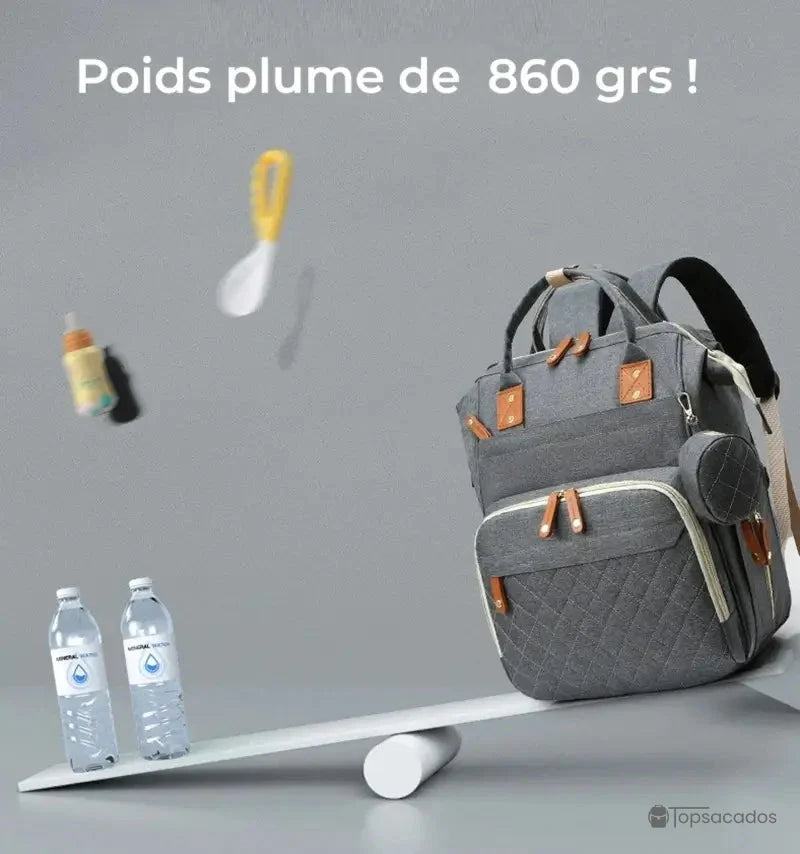 Sac à dos à langer avec port usb posé sur une balance en équilibre avec deux bouteilles d’eau, démontrant sa légèreté de 860 grammes, sur fond gris épuré.