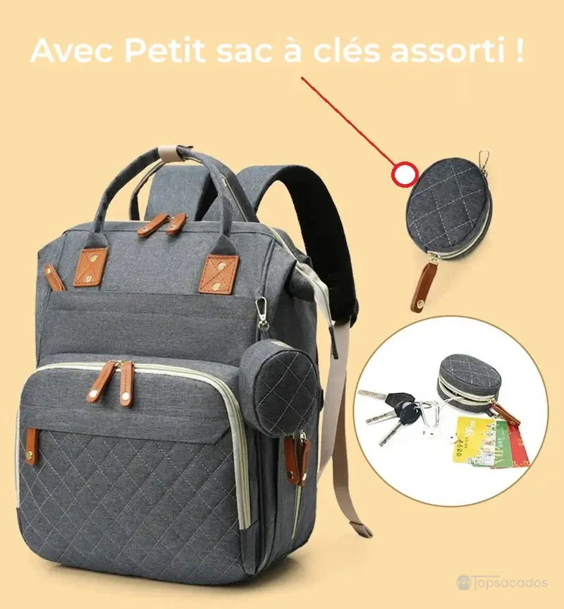 Sac à dos à langer avec port usb avec petit sac à clés assorti, suspendu sur le côté et zoomé avec contenu visible, sur fond beige.