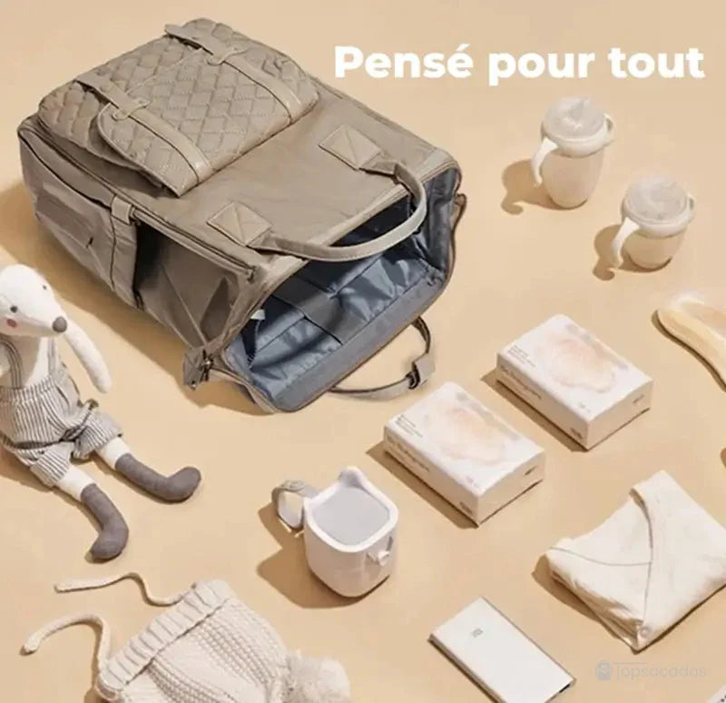 Sac à dos à langer multifonctions ouvert avec accessoires de puériculture posés autour, illustrant sa grande capacité et son organisation parfaite.