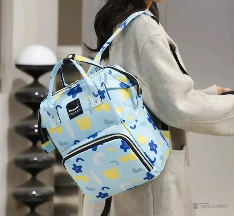 Sac à dos à langer porté en bandoulière par une femme en manteau gris, illustrant le confort d'utilisation et la polyvalence du transport.