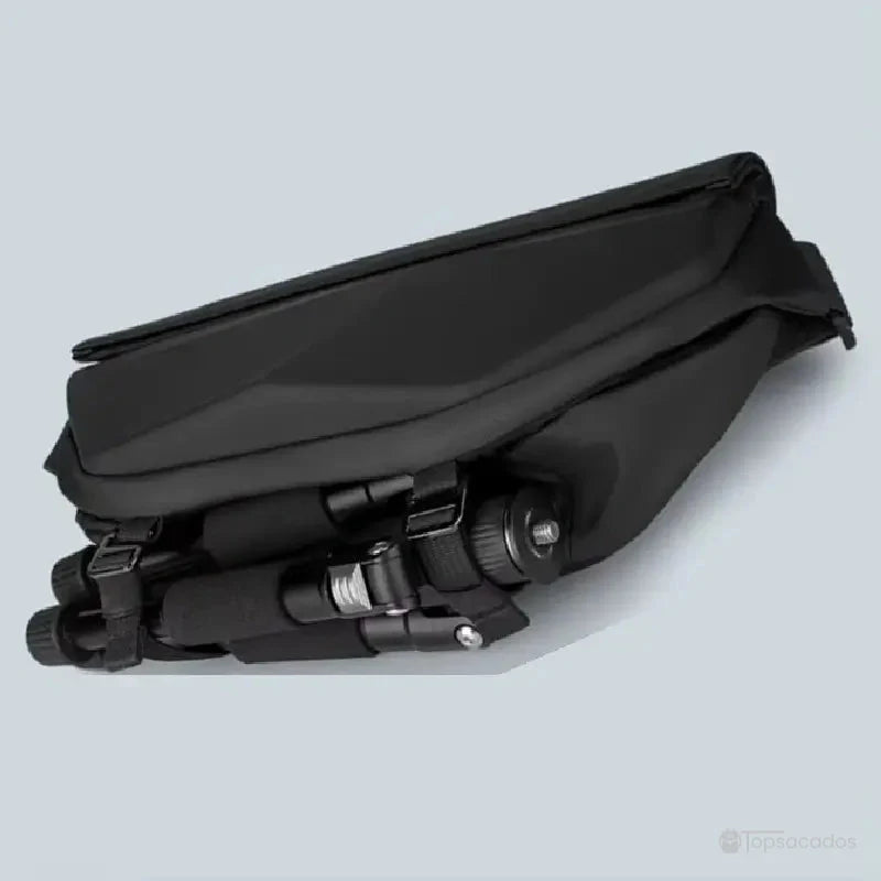 Sac à dos bandoulière avec trépied rangé dans le compartiment inférieur, sur fond gris clair.