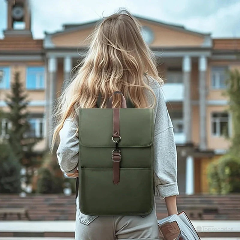 Sac à dos collège antivol fille vert porté par une étudiante blonde de dos, devant un bâtiment scolaire en arrière-plan.