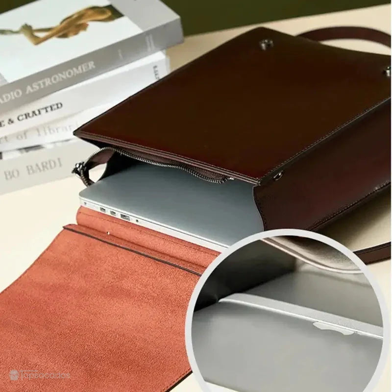Sac à dos cuir Femme avec rabat marron contenant un ordinateur portable dans une poche intérieure, posé sur un bureau avec des livres