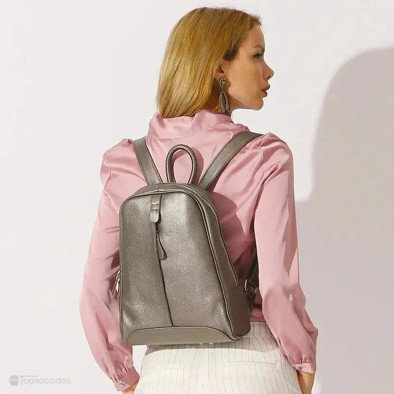 Sac à dos cuir femme tendance bronze porté par une femme vêtue d’une chemise rose, environnement en studio lumineux, ambiance mode urbaine.