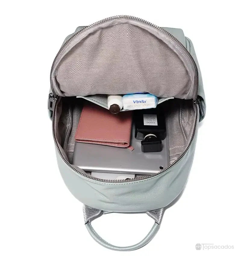Sac à dos cuir femme vert clair ouvert, intérieur gris avec plusieurs objets rangés comme un portefeuille rose, une crème et une tablette.