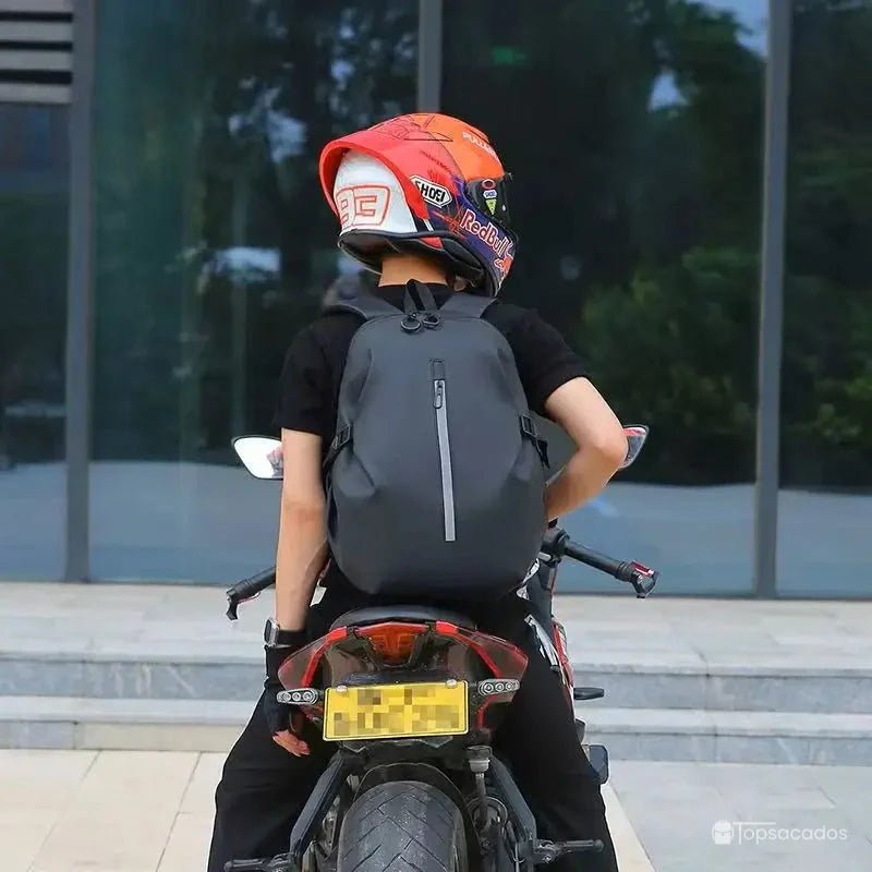 Sac à dos étanche pour moto porté par un motard sur route, vu de dos avec éclairage naturel urbain