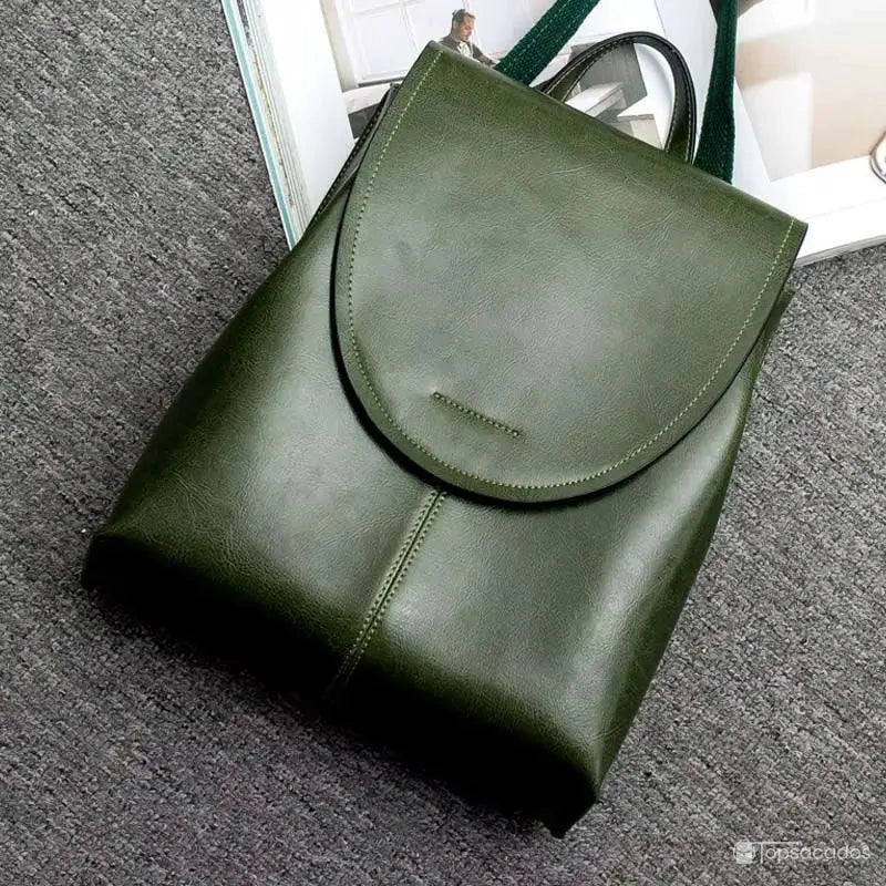 Sac à dos femme en cuir vert posé sur moquette grise à côté d’un magazine, mettant en valeur sa silhouette structurée.