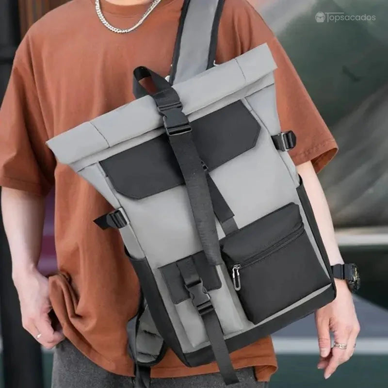 Sac à dos à fermeture enroulable porté en bandoulière par un homme en t-shirt marron, illustrant l’allure moderne et la tenue structurée du sac en usage urbain.