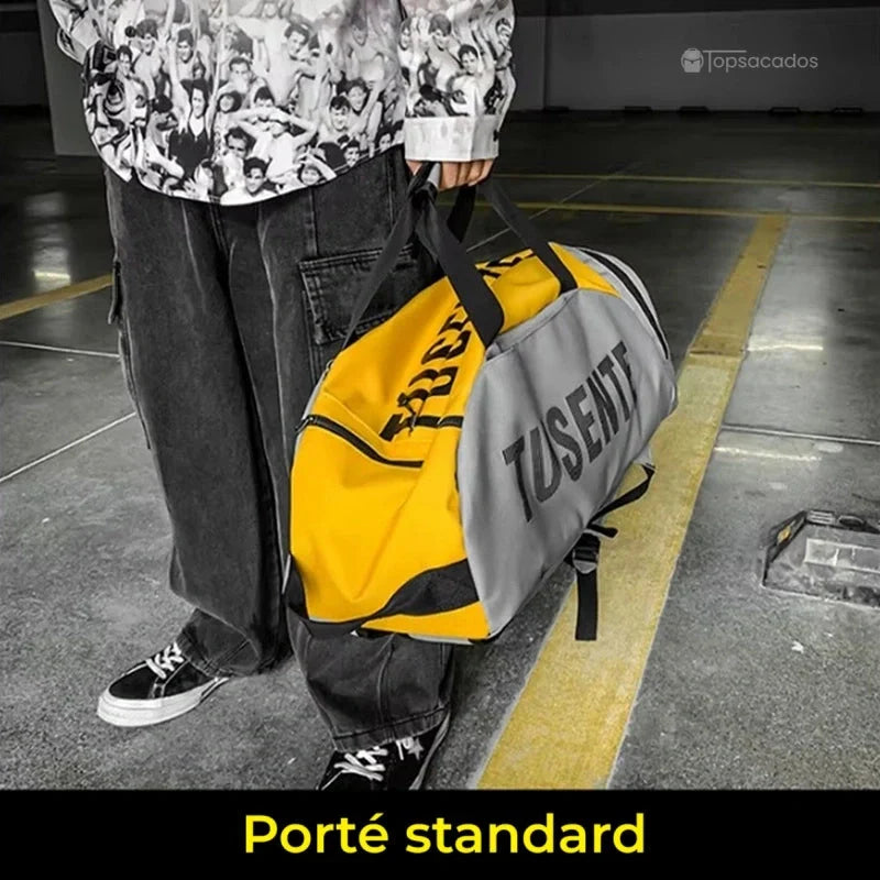 Sac à dos foot jaune et gris porté à la main façon sac de sport, en intérieur sur un parking.