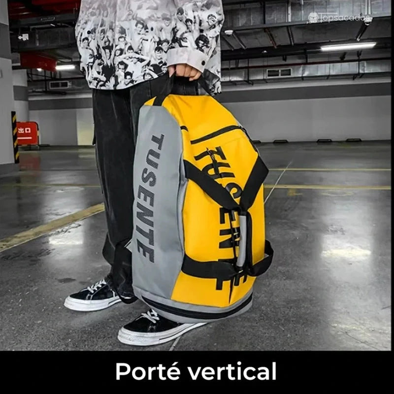 Sac à dos foot jaune et gris porté verticalement à la main dans un parking souterrain.