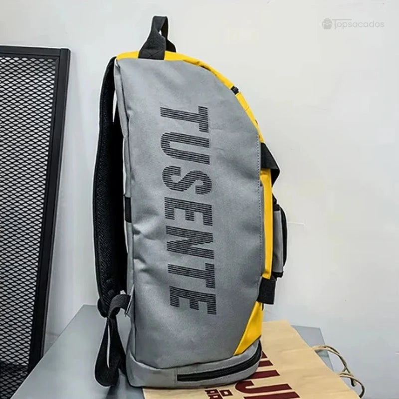 Sac à dos foot jaune et gris vu de profil posé sur un meuble, avec dos matelassé et bretelle visible.