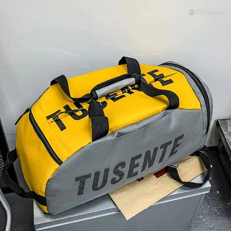 Sac à dos foot jaune et gris posé à plat sur une surface métallique, poignée renforcée bien visible.