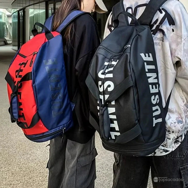Sac à dos foot rouge et noir et sac à dos noir portés par deux personnes en extérieur sur sol texturé clair.