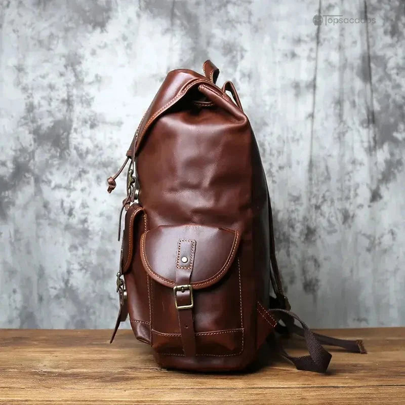 Sac à dos homme cuir brun foncé vu de profil posé sur une table avec fond gris