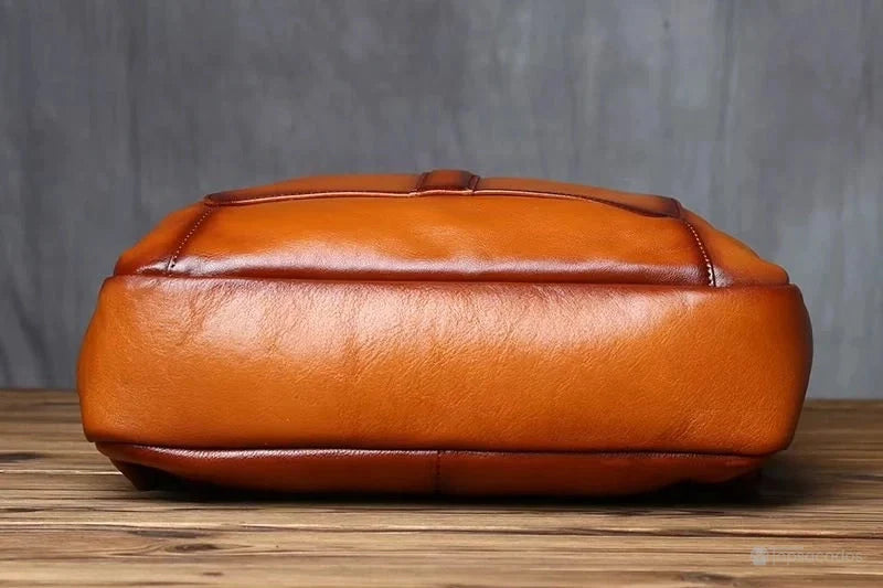 Sac à dos homme cuir marron vu de dessous, posé sur un sol en bois, montrant la qualité du cuir lisse et robuste.