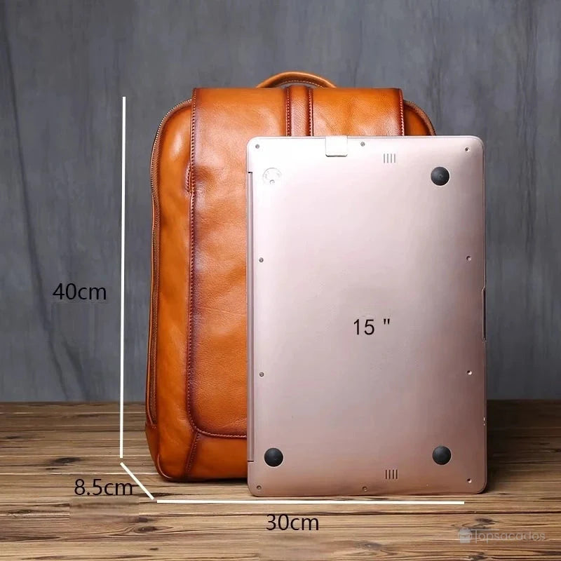 Sac à dos homme cuir marron comparé à un ordinateur 15 pouces pour illustrer ses dimensions pratiques, fond bois et mur gris.