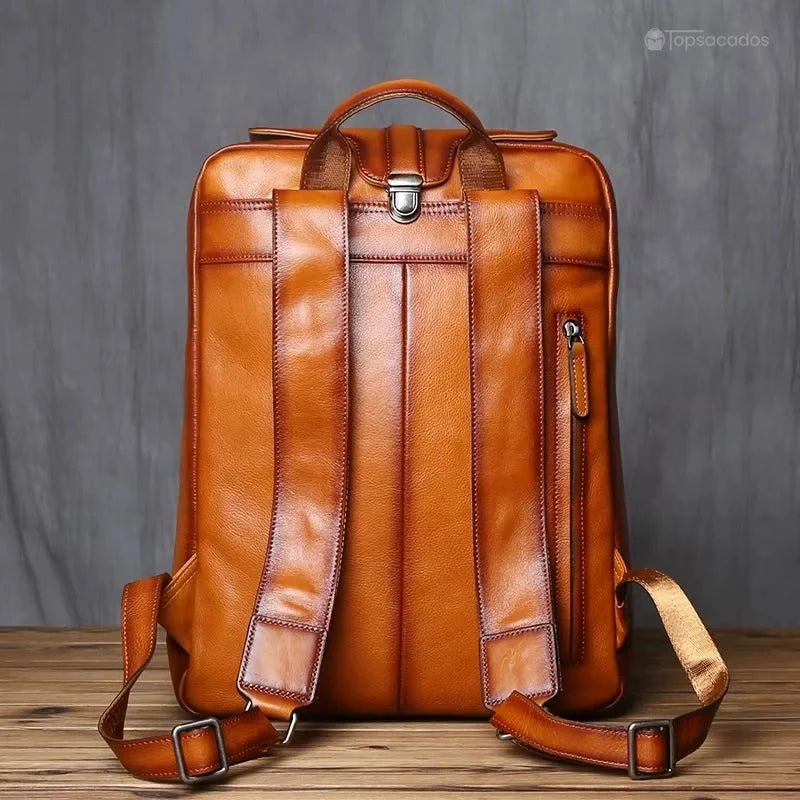 Sac à dos homme cuir marron vu de dos avec bretelles larges et poche zippée anti pickpocket, environnement intérieur bois et mur gris.