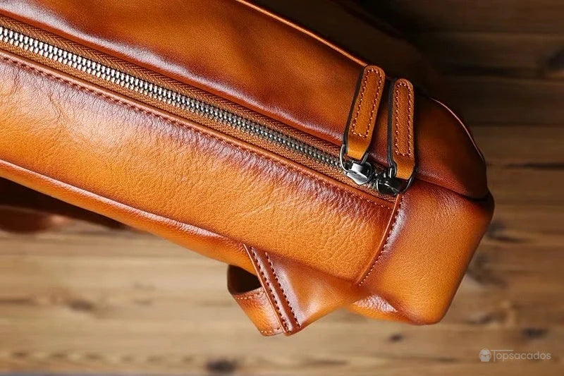 Sac à dos homme cuir marron gros plan sur la fermeture éclair en métal solide avec deux languettes en cuir marron, fond bois naturel.