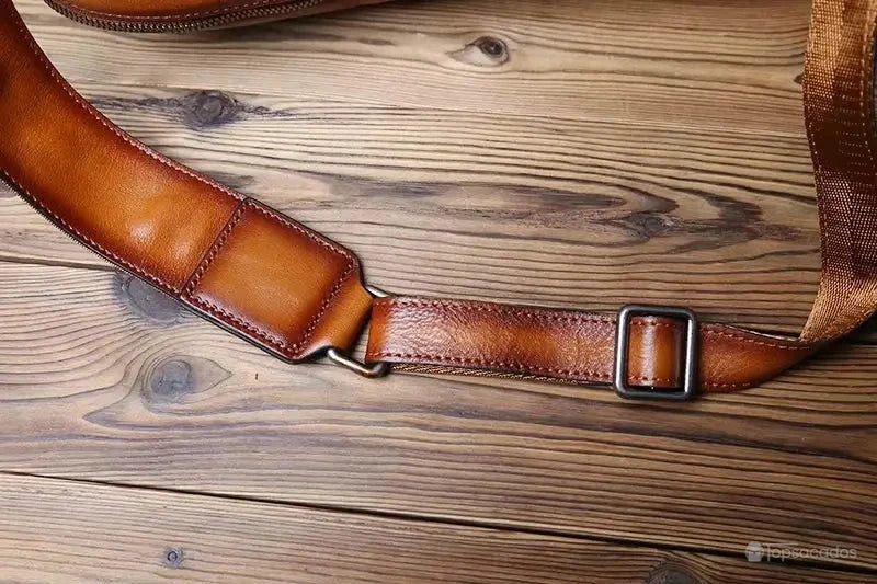 Sac à dos homme cuir marron zoom sur la sangle ajustable en cuir et nylon, posée sur un sol en bois texturé.