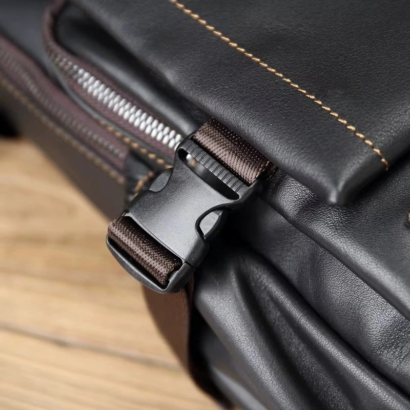 Sac à dos homme cuir noir zoom sur boucle de fermeture en plastique noir et sangle marron sur fond de table en bois.