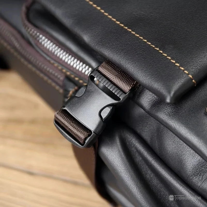 Sac Ă  dos homme cuir noir zoom sur boucle de fermeture en plastique noir et sangle marron sur fond de table en bois.