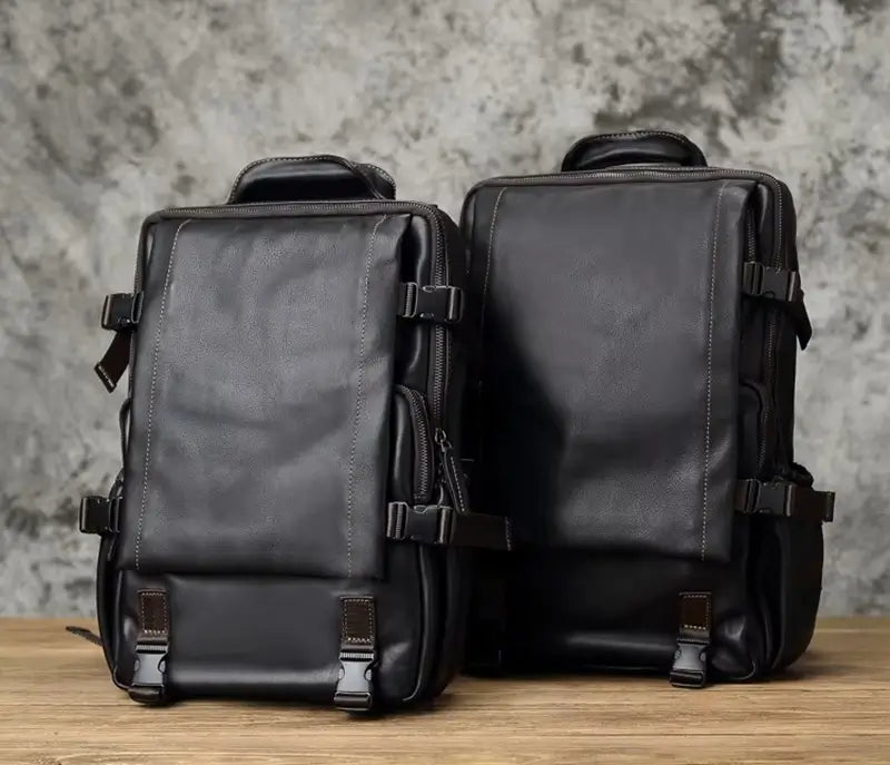 Sac à dos homme cuir noir duo de sacs posés sur une table en bois, montrant les deux tailles disponibles, fond en béton gris.