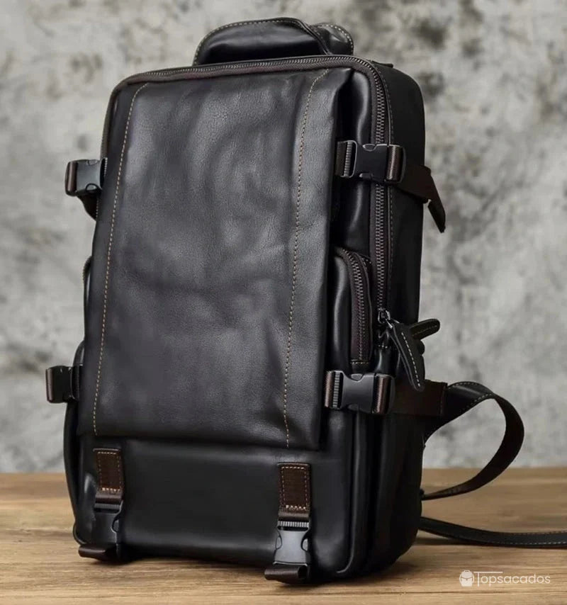 Sac à dos homme cuir noir rectangulaire en cuir lisse, posé sur une table en bois avec fond en béton gris.