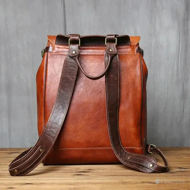 Sac à dos homme cuir vintage vu de dos, montrant les bretelles larges et renforcées en cuir foncé, posé sur une table boisée.
