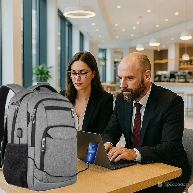Sac à dos Homme ville gris en usage professionnel, posé sur une table de café moderne avec recharge de smartphone.