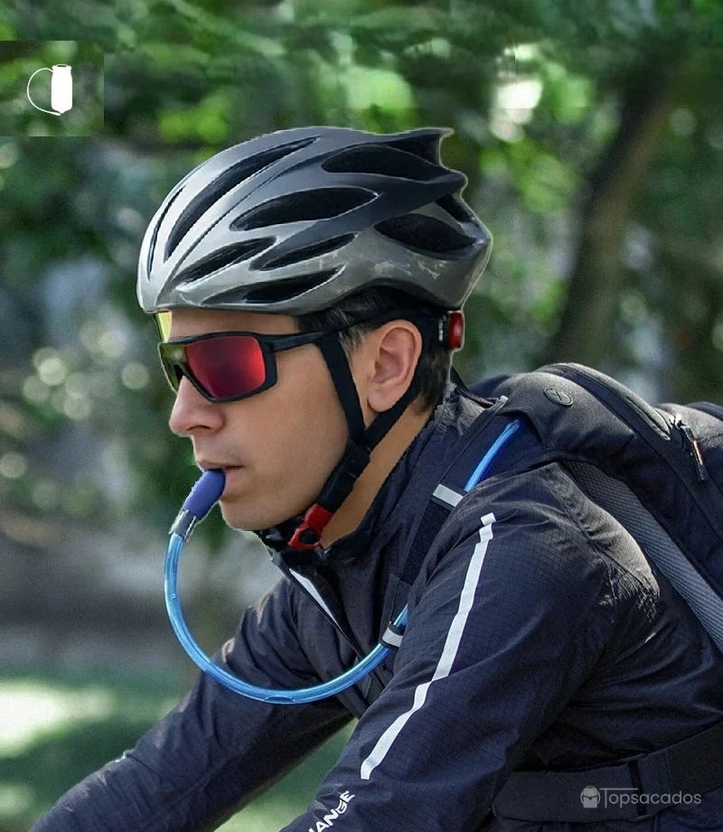 sac à dos hydratation 2 litres porté par un cycliste buvant via le tuyau bleu intégré à la poche à eau, en pleine activité, casque et lunettes de sport