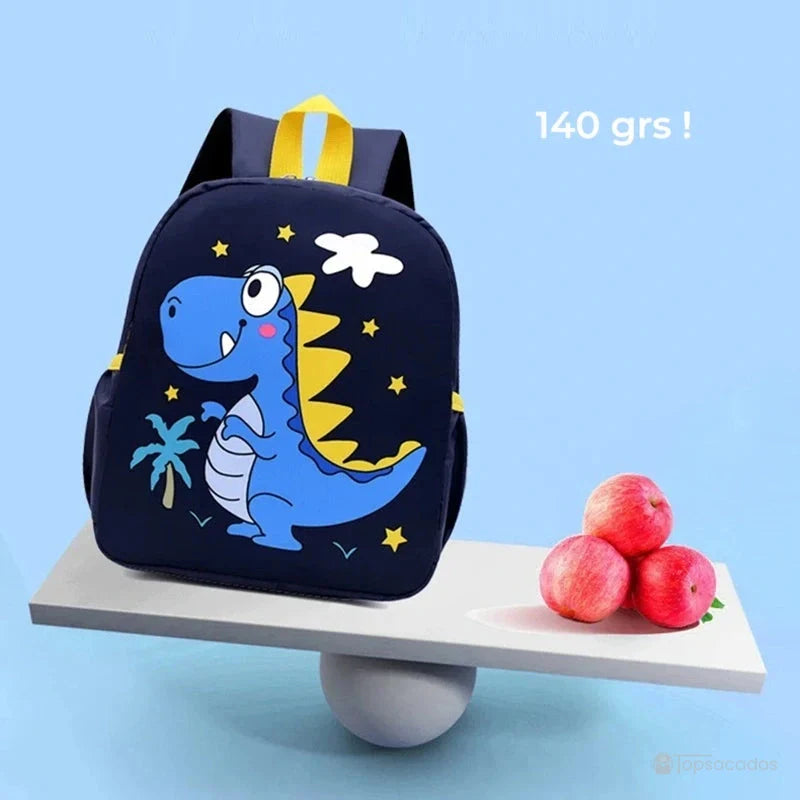 Sac à dos maternelle dinosaure bleu posé sur une balance face à trois pommes rouges, mettant en valeur sa légèreté de 140 grammes