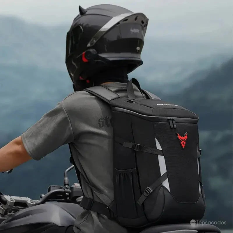 Sac a dos moto étanche porté par un motard en conduite, vue latérale sur route boisée avec sac noir équipé de bandes réfléchissantes pour la sécurité.