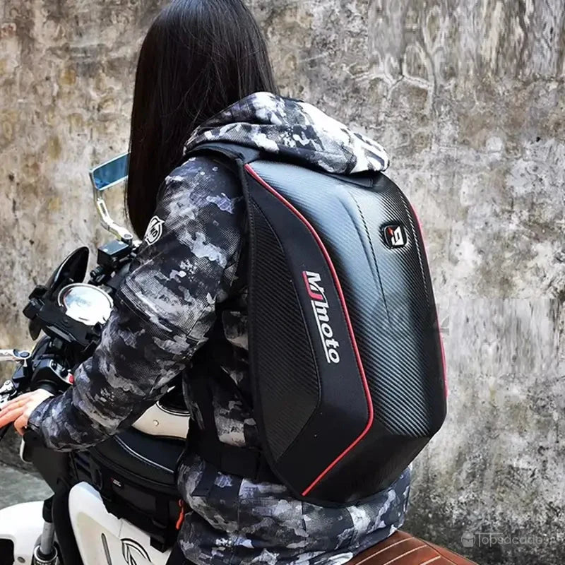 Sac à dos moto en fibre de carbone porté par une motarde sur sa moto, contre un mur en béton, illustrant l'utilisation en situation réelle.