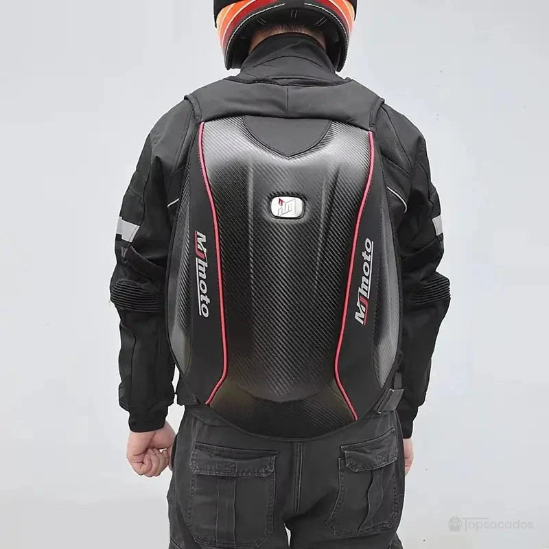 Sac à dos moto en fibre de carbone vu de dos, porté par un motard en équipement complet, casque orange et tenue noire avec bandes réfléchissantes.