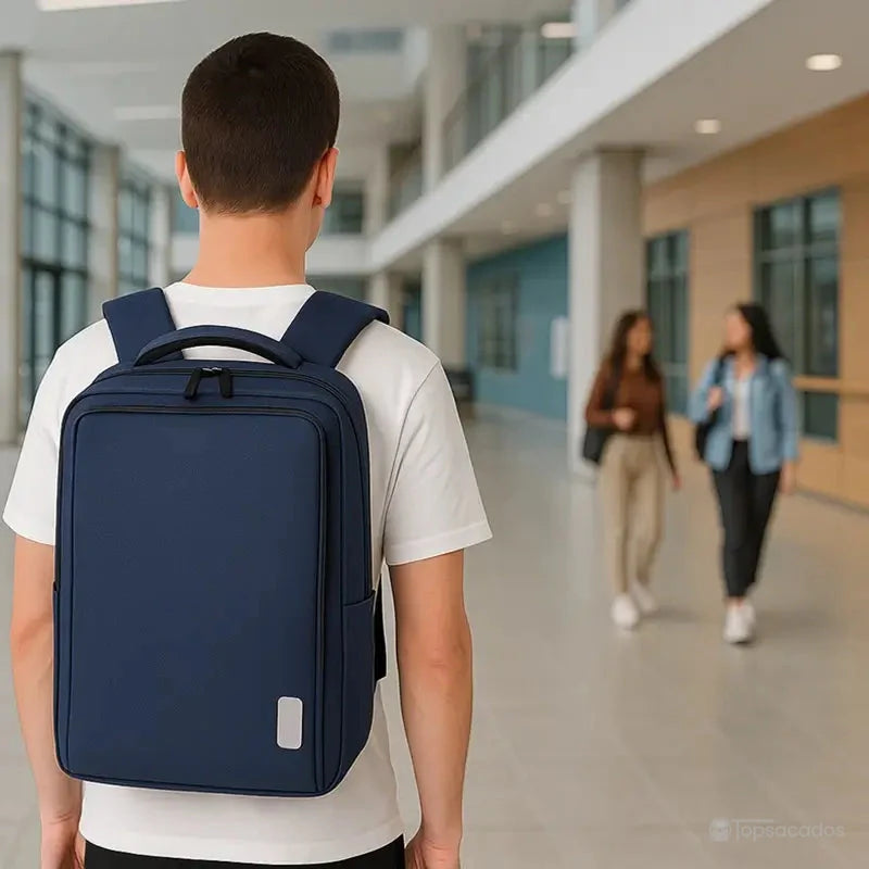 Sac à dos ordinateur Homme porté dans un hall universitaire moderne, vu de dos sur un jeune homme en t-shirt blanc.