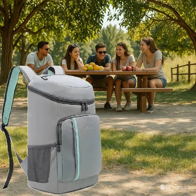 Sac à dos picnic isotherme gris posé au premier plan d’un pique-nique en plein air, devant un groupe d’amis assis à une table.
