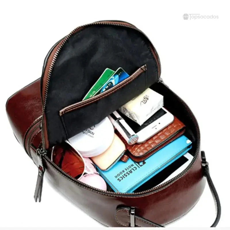 Sac à dos pour femme en cuir ouvert, rempli d’objets du quotidien comme un téléphone, portefeuille, lunettes et carnet.