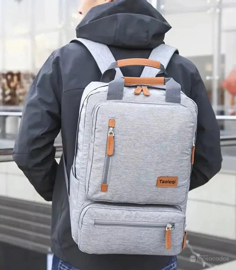 Sac à dos pour lycéen gris clair porté par un adolescent en tenue noire, en extérieur urbain.