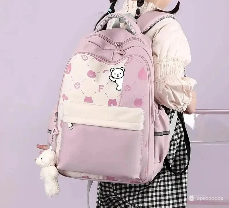 Sac à dos primaire fille rose porté par une écolière vue de dos, sur fond violet clair.